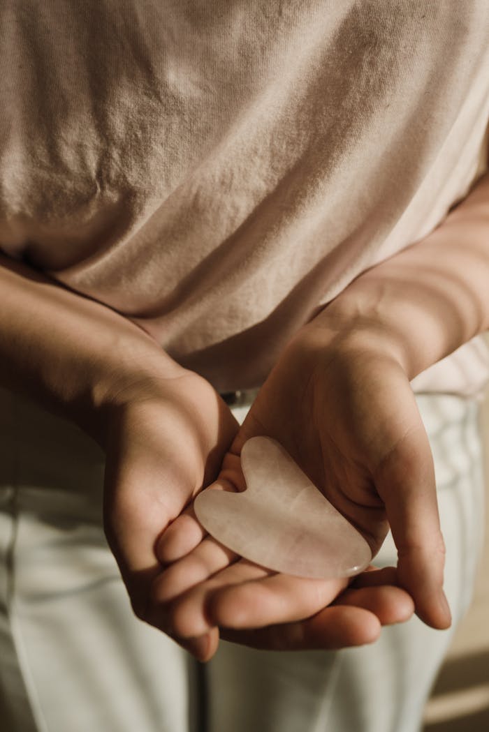 Close-up of hands gently cradling a heart-shaped gua sha stone tool used in skincare routines.